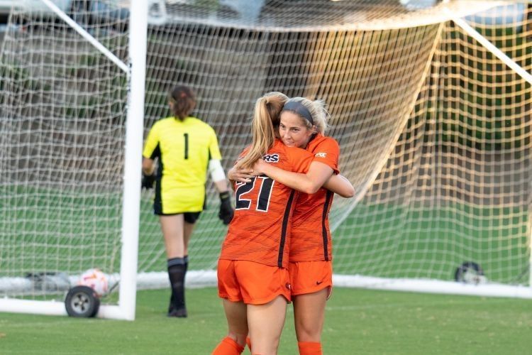 two soccer players hug while standing on the field