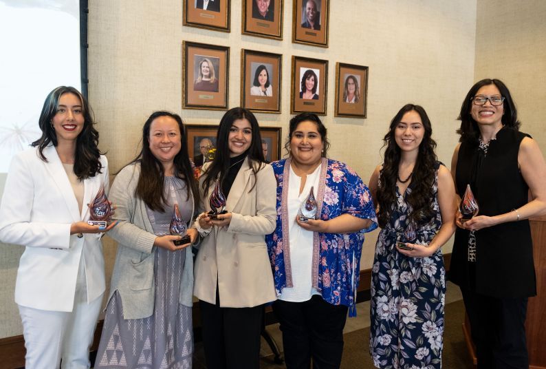 Six women stand together holding awards at ceremony