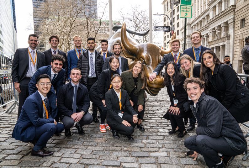 students stand next to the bull of Wall Street statue