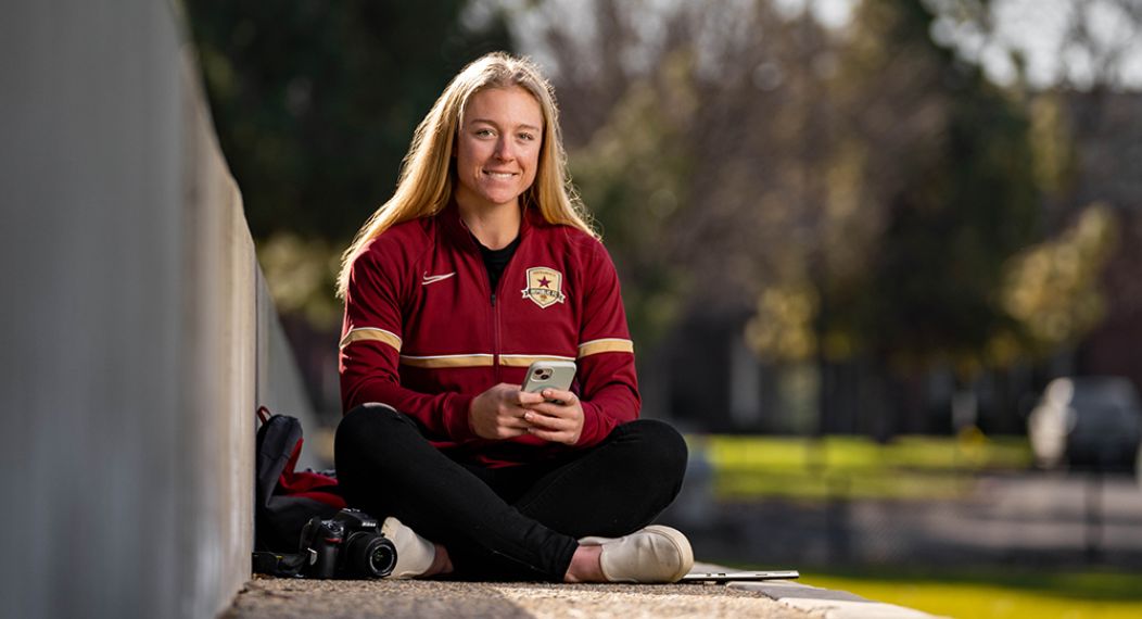 college student wearing a sport jersey sits on a soccer field