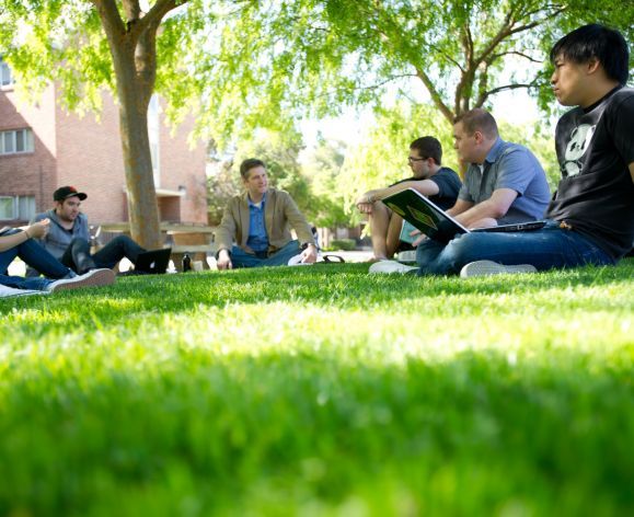 students sitting on campus lawn with professor